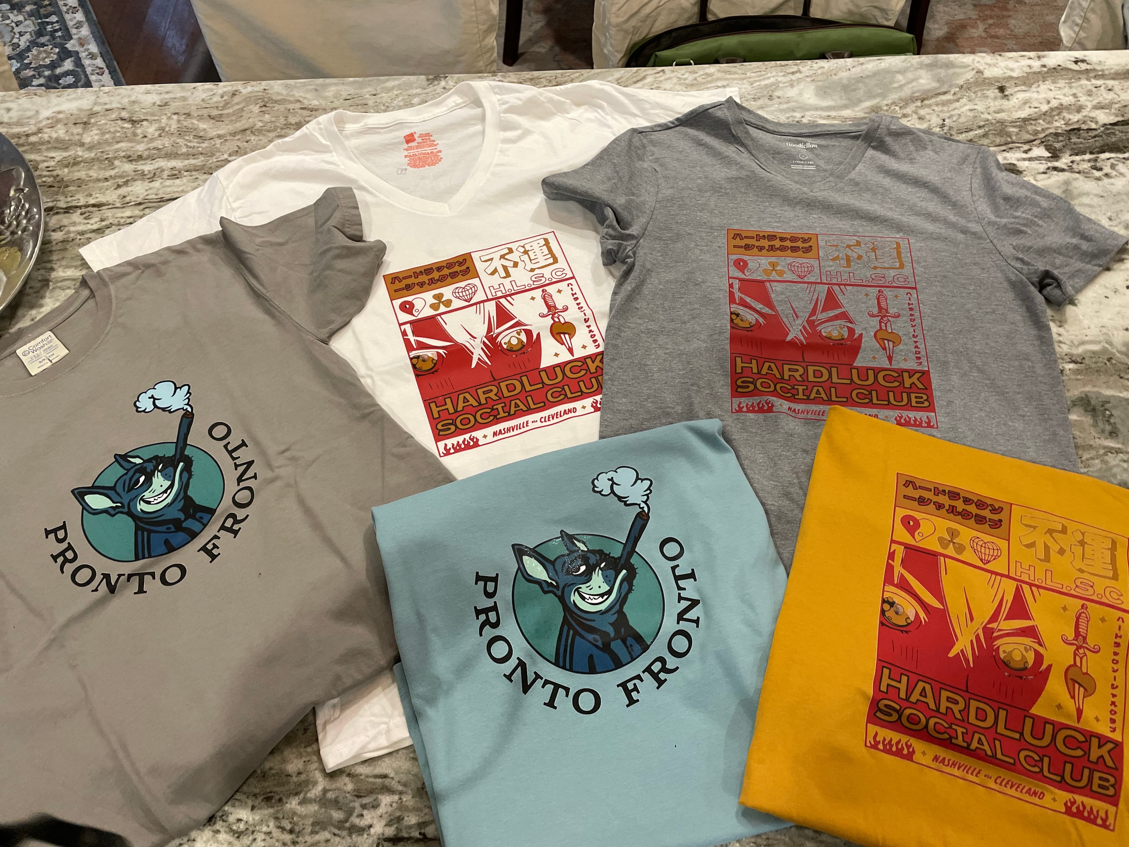 A real stack of printed Hardluck Social Club t-shirts laid out on a counter